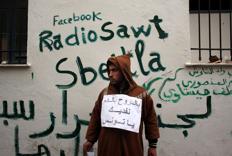 A man stands next to Facebook graffiti as Tunisians continued their demonstrations outside Prime Minister Mohammed Ghannouchi's offices in Government Square Tunis on January 25, 2011 in Tunis, Tunisia. The government square became a makeshift camp as prot