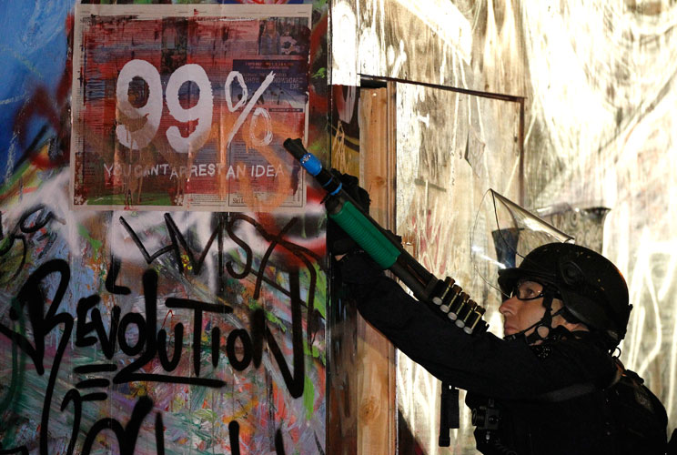 A Los Angeles police officer points his weapon to demonstrators in a tree as police officers dismantle the Occupy LA encampment following a raid by LAPD in the early house of November 30, 2011 in Los Angeles, California.