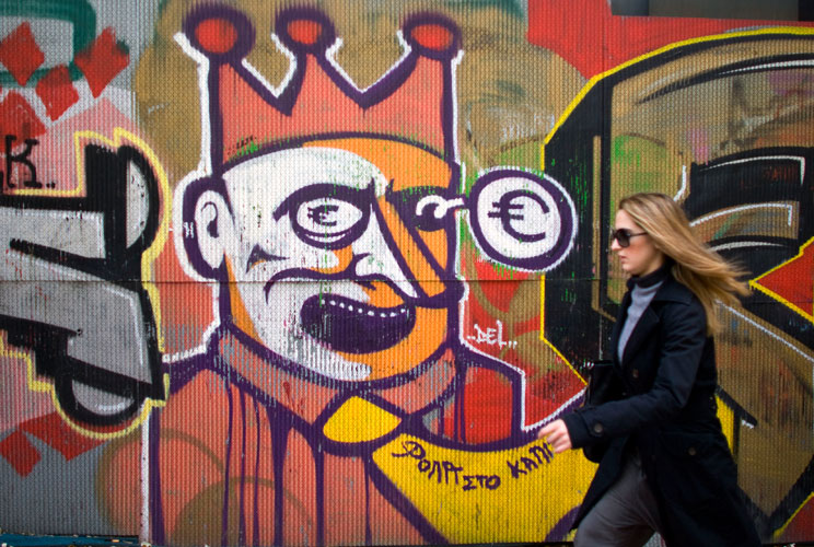 A woman walks past graffiti displayed on a building on December 6, 2011 in Athens, Greece. Graffiti artists throughout the city are expressing the effects of austerity measures that have plagued the community as Greece continues to struggle in debt while